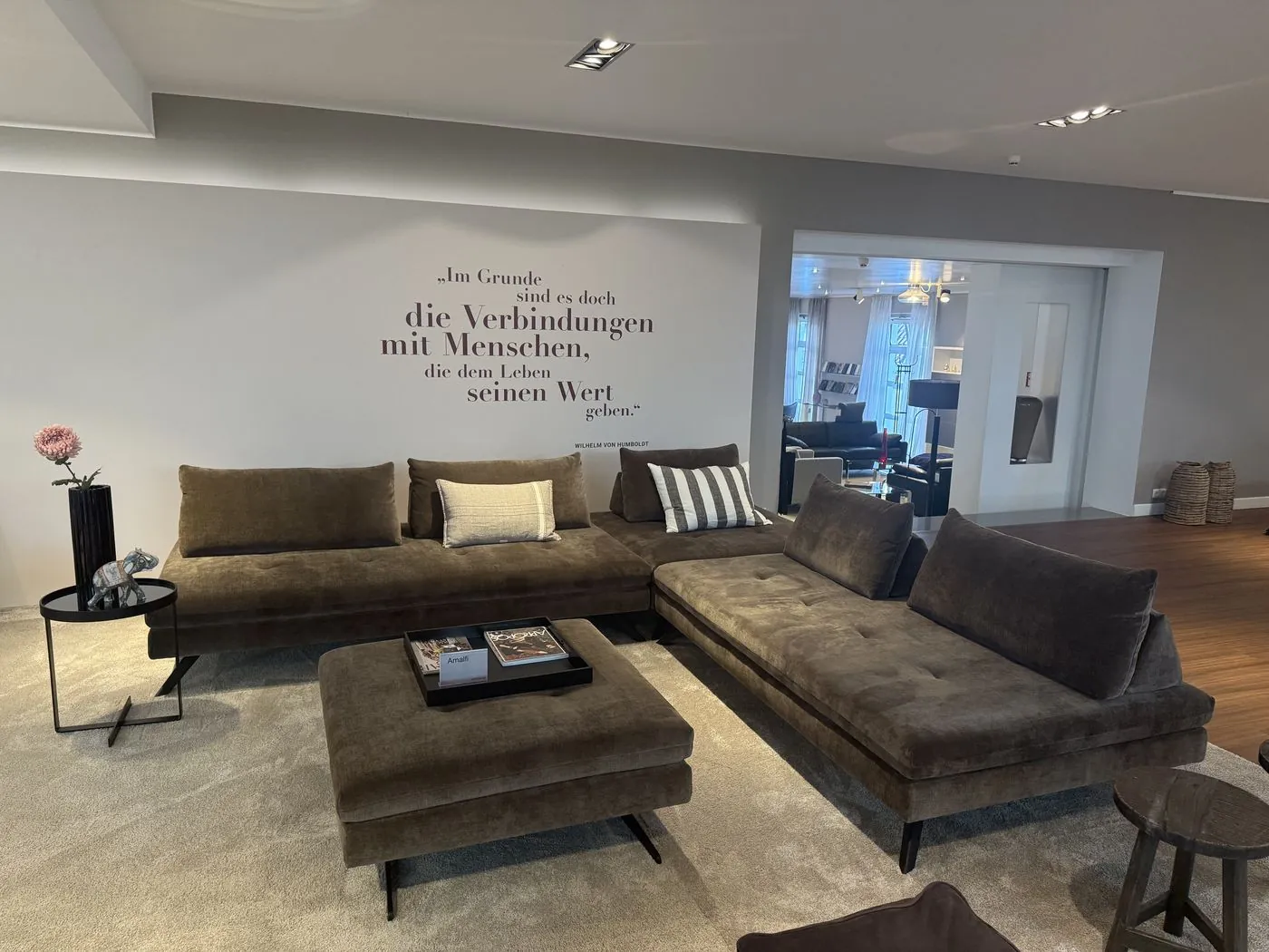 Ecksofa in Olivbraun mit Hocker vor dem Wandspruch