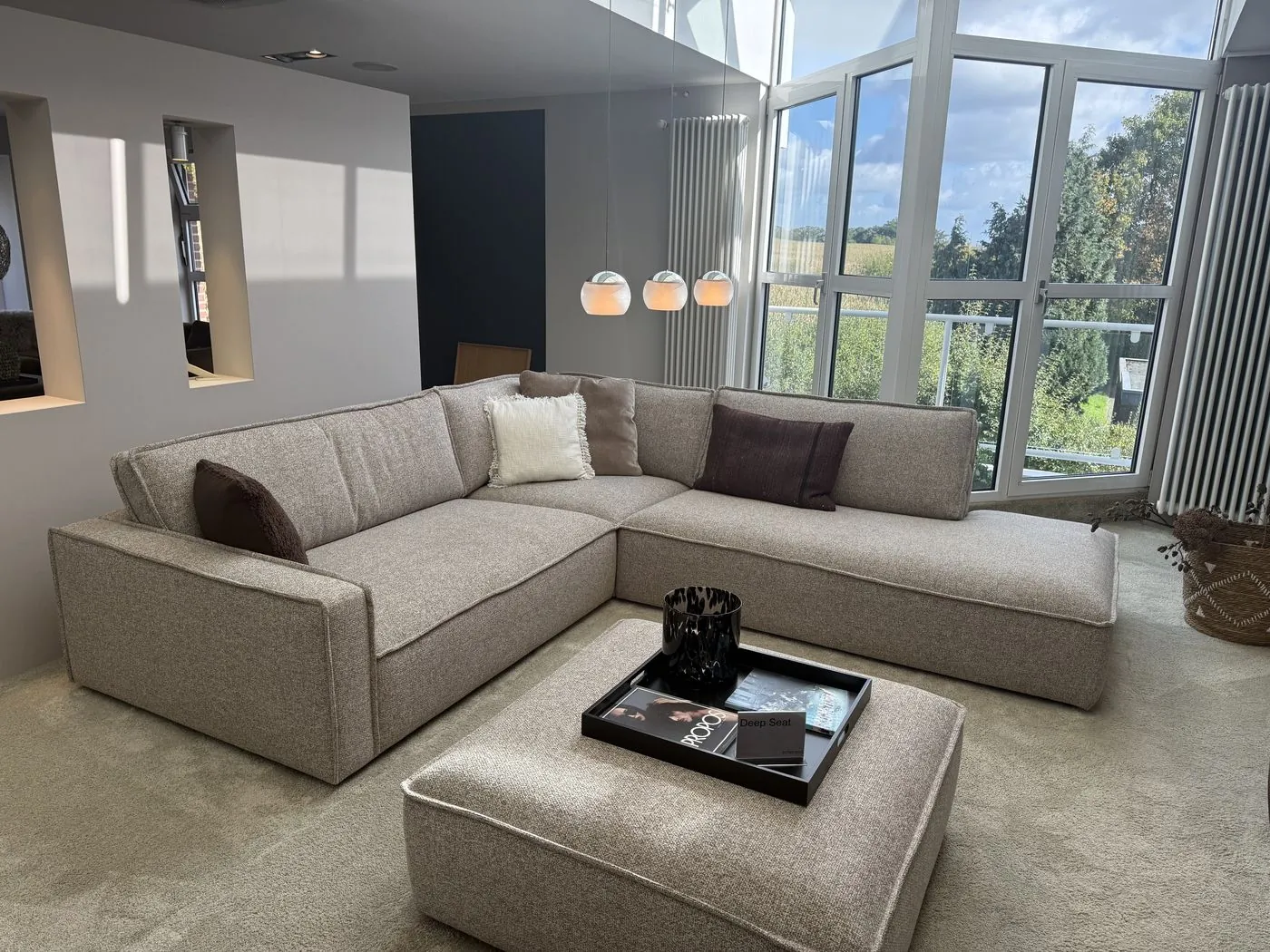 Ecksofa in Grau-Beige vor bodentiefen Fenstern