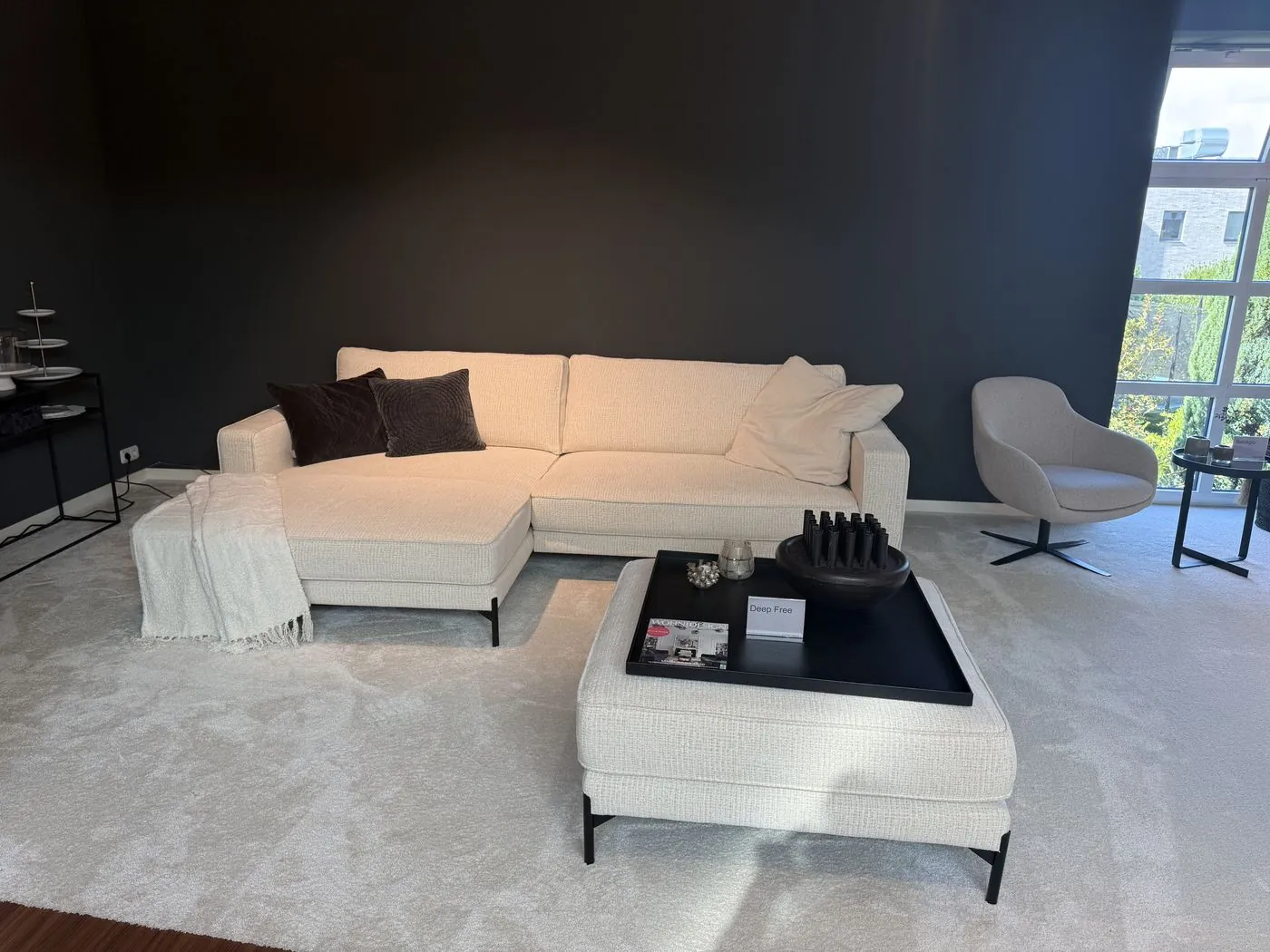 Weißes Ecksofa mit Hocker vor dunkler Wand